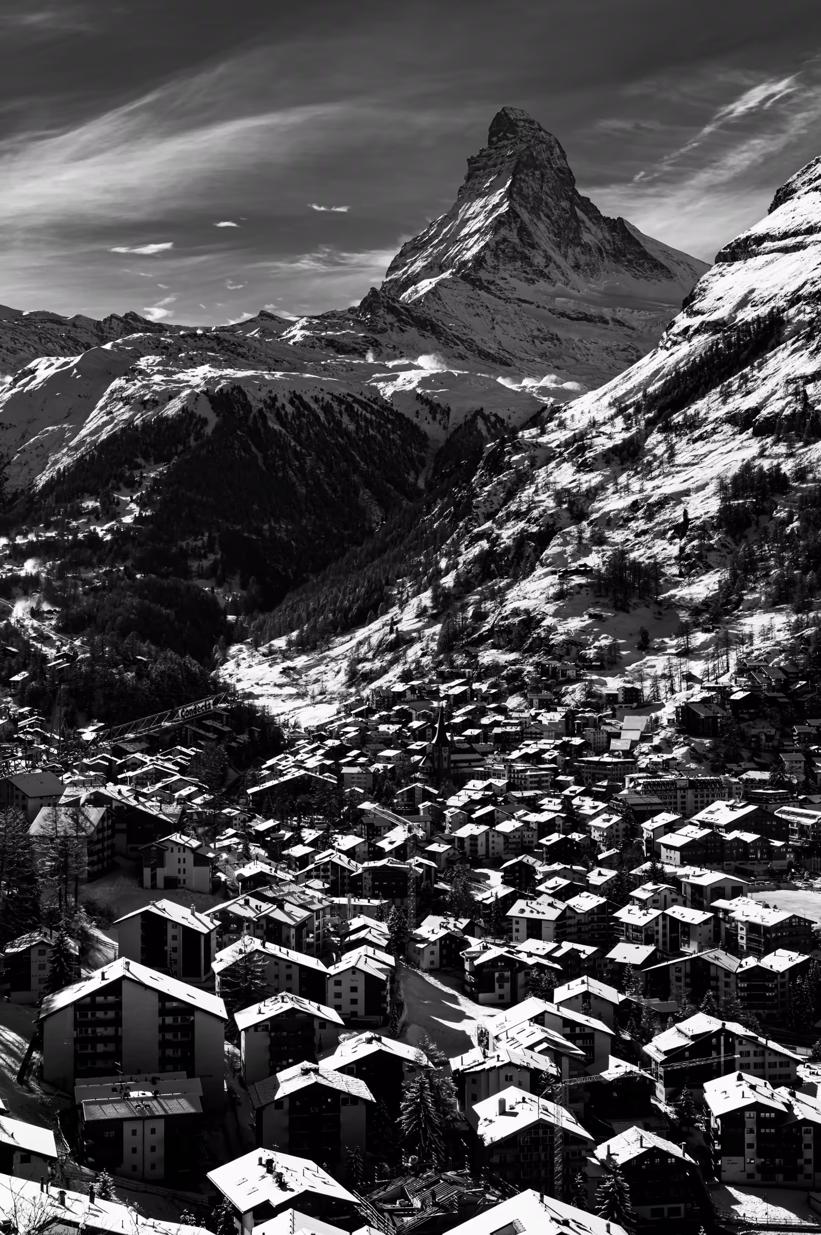 High-contrast, black and white photograph of the snow-covered village of Zermatt, with the iconic Matterhorn mountain in the background.
